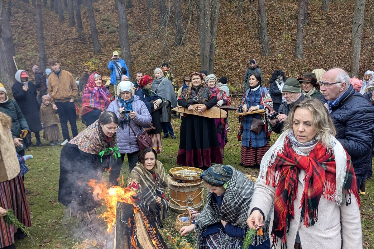 Tautiniais drabužiais vilkintys lankytojai prie Mārtiņdiena laužo Latvijos etnografiniame atviro oro muziejuje, Rīga.