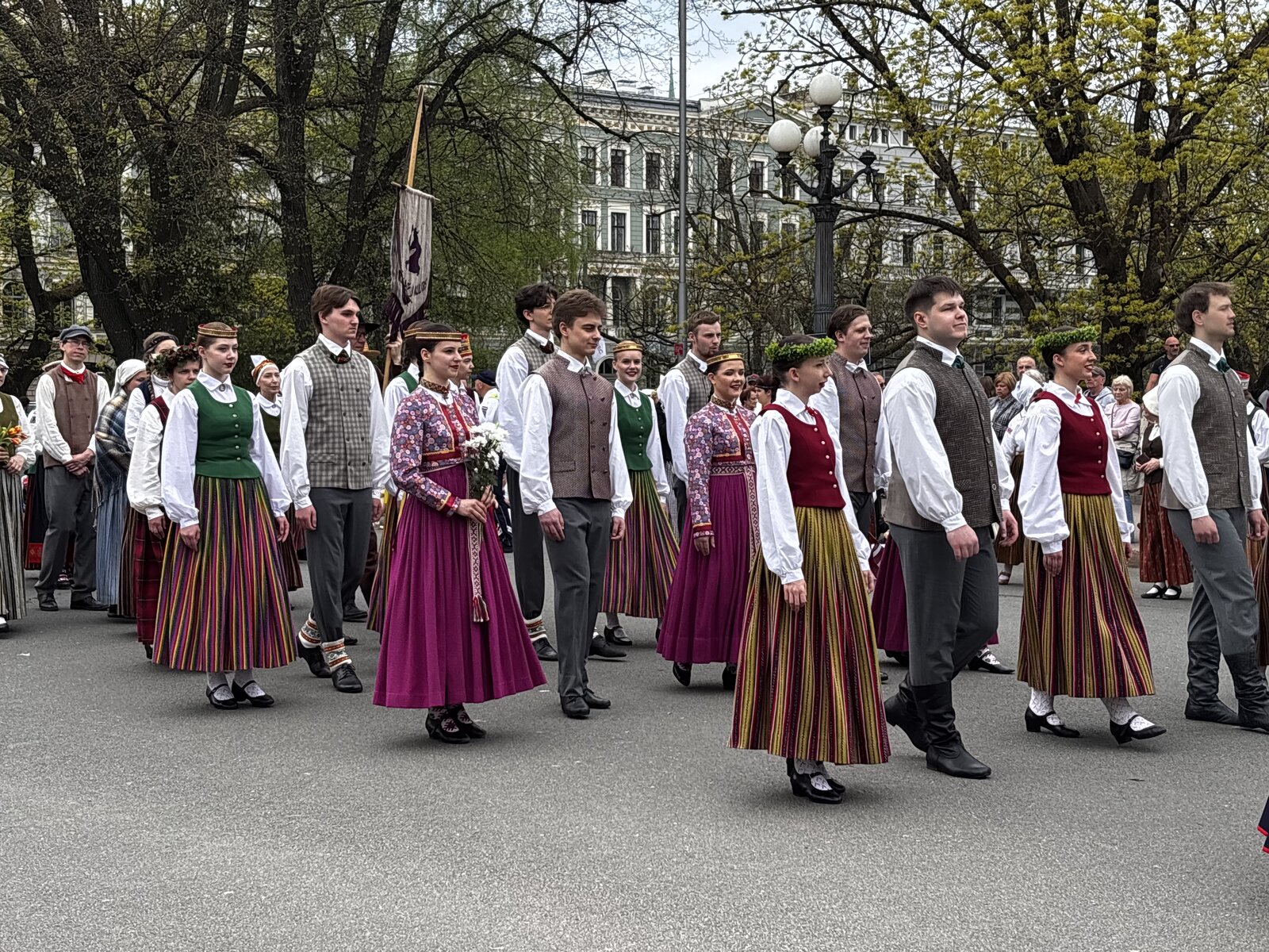 Tautiniais kostiumais vilkinčių žmonių procesija pro Brīvības piemineklis su iškelta Latvijos vėliava, Rīga, gegužės 4 d.