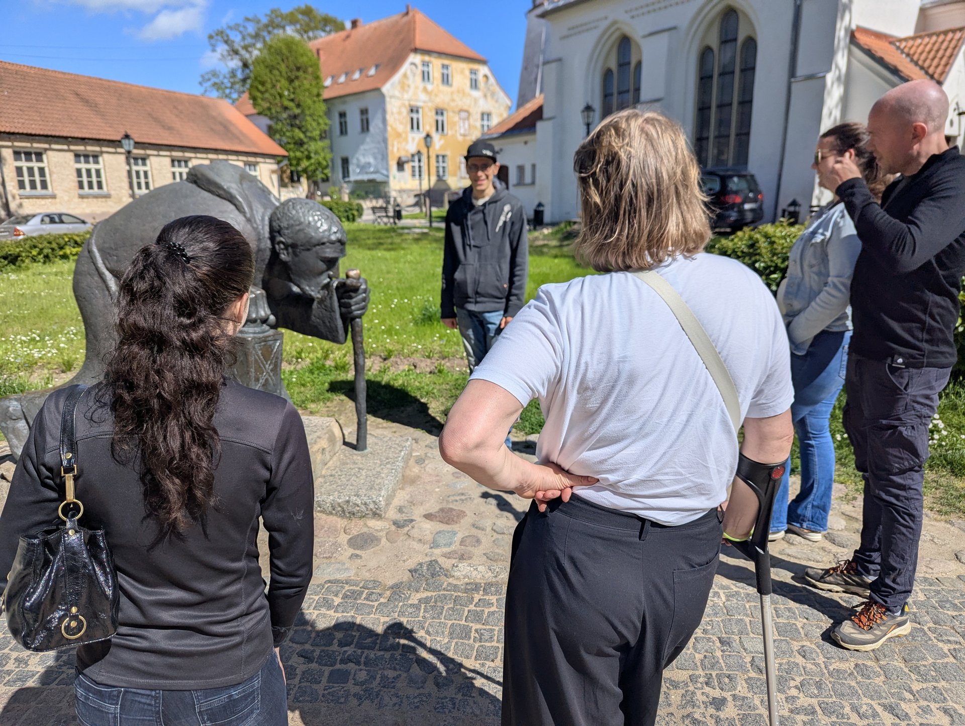 Grupė aplink bronzinę piligrimo skulptūrą Cēsių senamiestyje